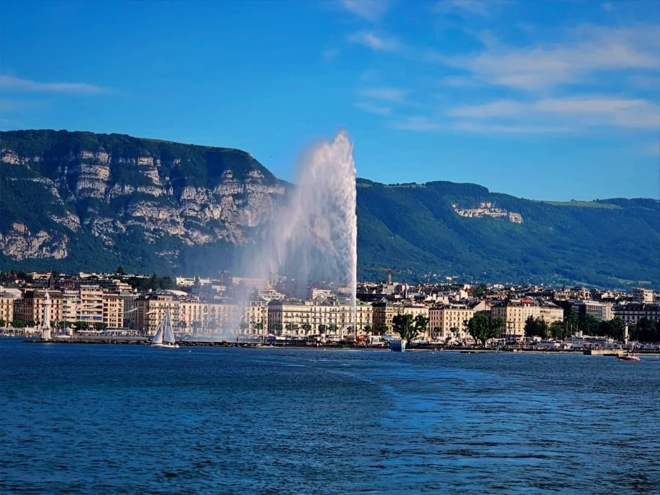 The Jet d'Eau fountain shoots up water before Geneva's skyline and Mont Salève